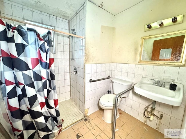 bathroom with a stall shower, toilet, a wainscoted wall, a sink, and tile walls