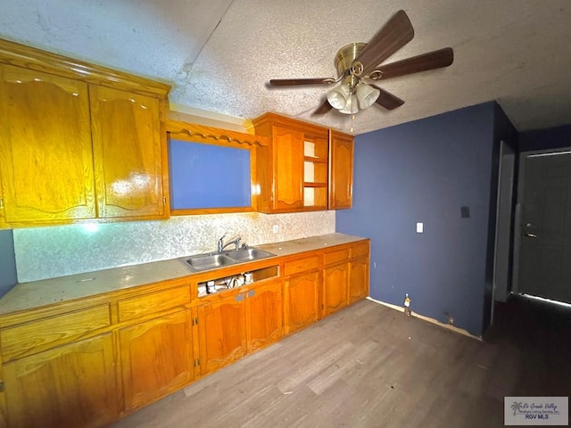 kitchen with a textured ceiling, a sink, light wood-type flooring, decorative backsplash, and brown cabinetry