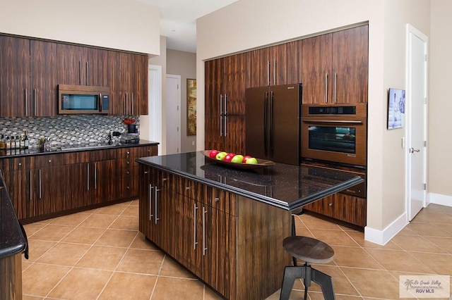 kitchen featuring tasteful backsplash, dark stone counters, stainless steel appliances, a kitchen island, and a breakfast bar area