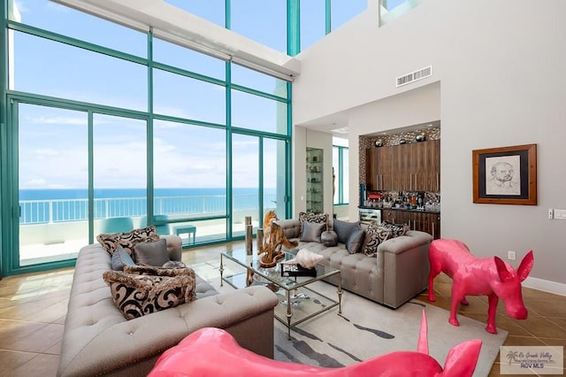 tiled living room featuring a towering ceiling, a water view, and a healthy amount of sunlight