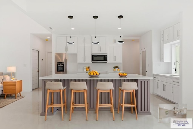 kitchen with appliances with stainless steel finishes, a breakfast bar, white cabinets, hanging light fixtures, and a center island