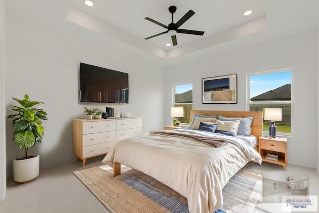 bedroom featuring a raised ceiling, ceiling fan, and multiple windows