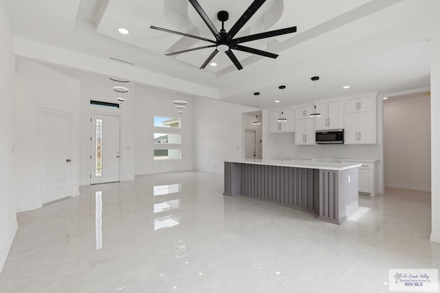 kitchen with ceiling fan, white cabinetry, a spacious island, a tray ceiling, and decorative light fixtures