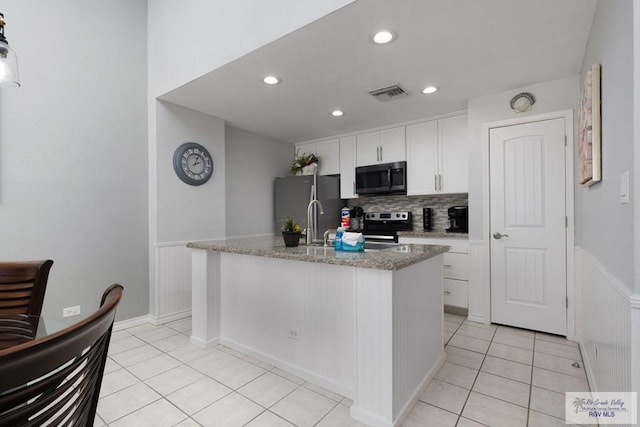 kitchen featuring white cabinets, light tile patterned floors, an island with sink, light stone counters, and stainless steel appliances