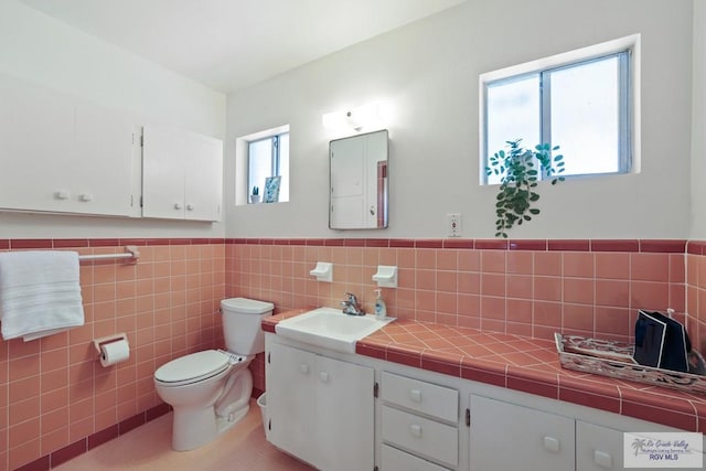 bathroom with tile walls, wainscoting, toilet, and vanity