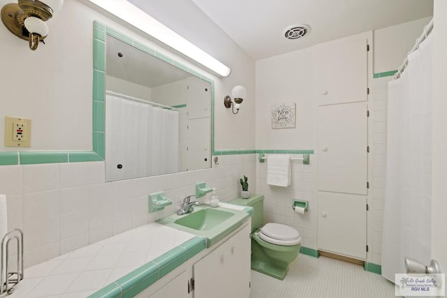full bathroom featuring tile patterned floors, tile walls, toilet, vanity, and curtained shower