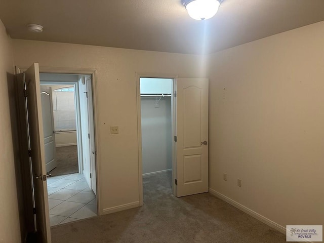 unfurnished bedroom featuring light carpet, baseboards, a spacious closet, and a closet