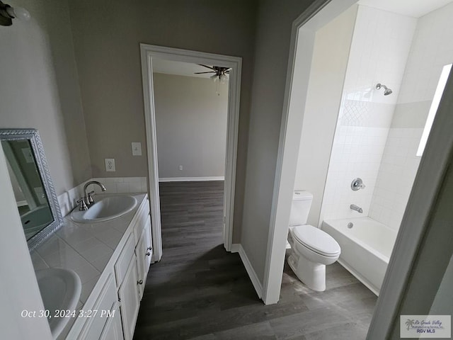bathroom featuring wood finished floors, ceiling fan, toilet, double vanity, and baseboards