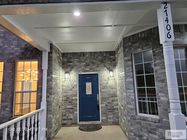 view of exterior entry featuring a porch and brick siding