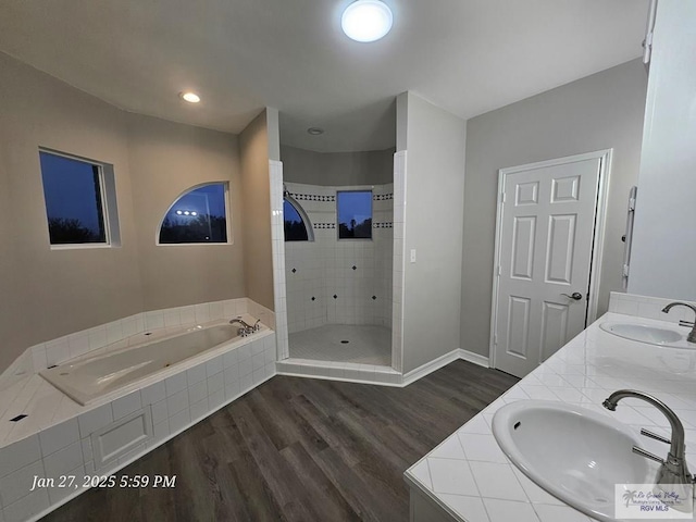 bathroom featuring wood finished floors, a garden tub, a stall shower, baseboards, and double vanity