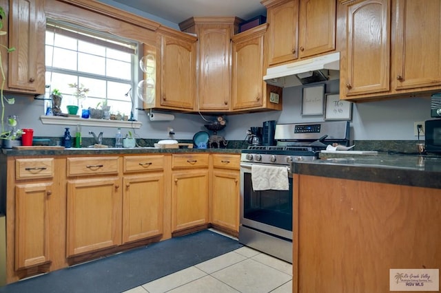 kitchen with stainless steel gas stove, light tile patterned floors, dark countertops, and under cabinet range hood