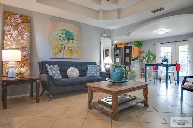 living area with arched walkways, french doors, a raised ceiling, and light tile patterned floors