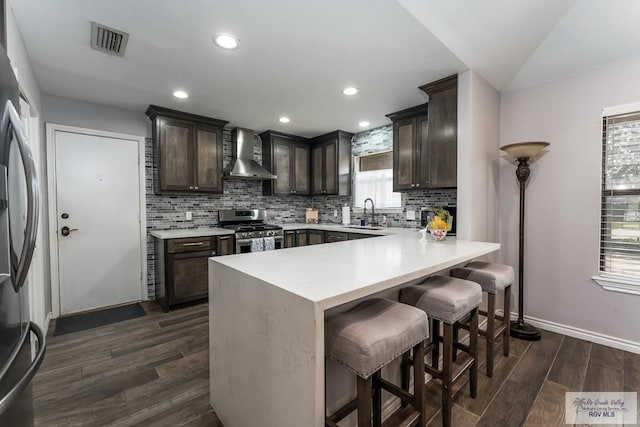 1916 Loquat Dr, Harlingen, TX 78552 - kitchen with wall chimney exhaust hood, stainless steel appliances, baseboards, dark brown cabinetry, and a peninsula