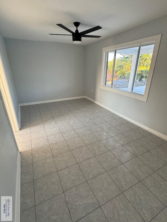 spare room with dark tile patterned flooring, ceiling fan, and baseboards