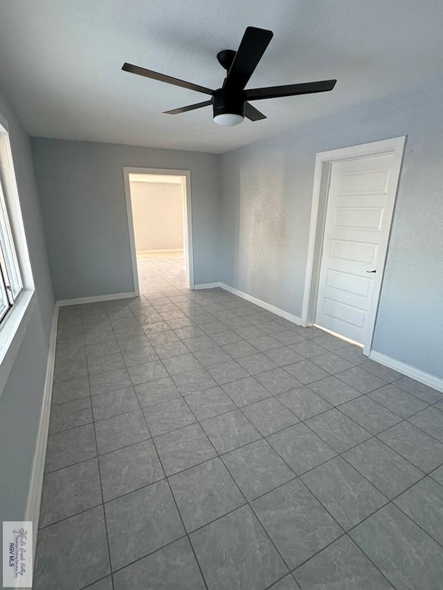 empty room featuring ceiling fan, tile patterned flooring, and baseboards