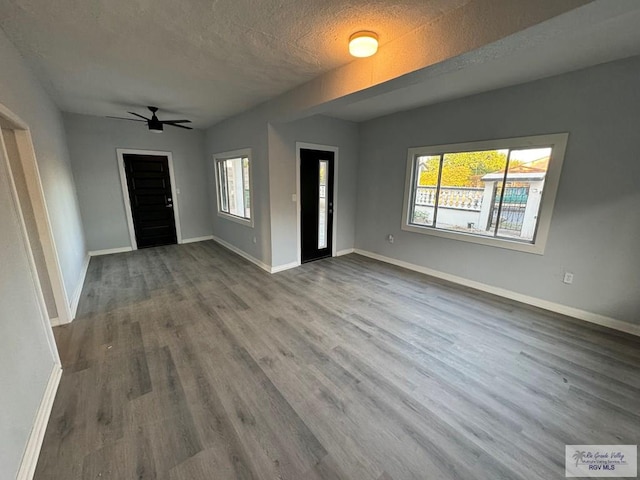 interior space featuring a ceiling fan, a textured ceiling, baseboards, and wood finished floors