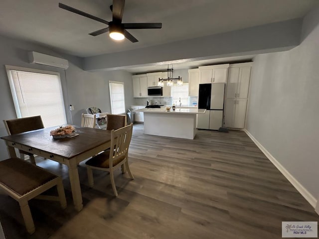 dining space featuring dark wood-style floors, a wall unit AC, a ceiling fan, and baseboards