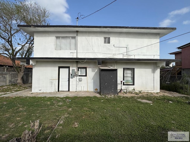 back of property featuring stucco siding, fence, and a yard