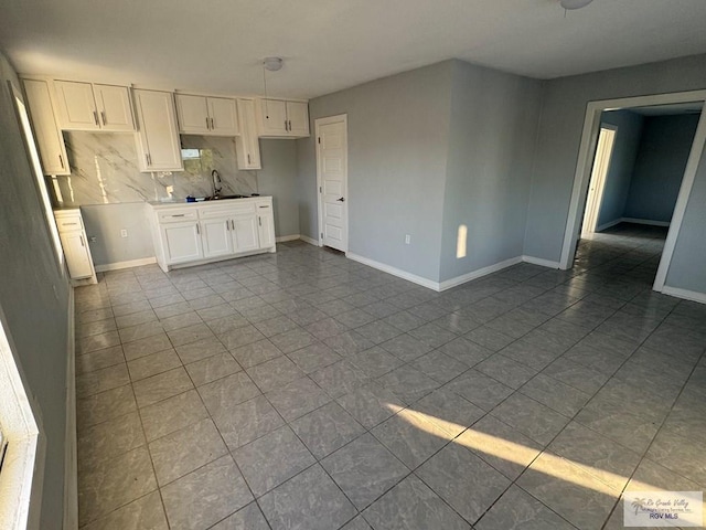 kitchen with dark tile patterned flooring, a sink, baseboards, white cabinets, and backsplash