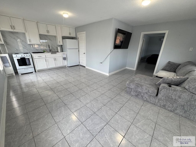 kitchen with electric stove, freestanding refrigerator, open floor plan, white cabinets, and a sink