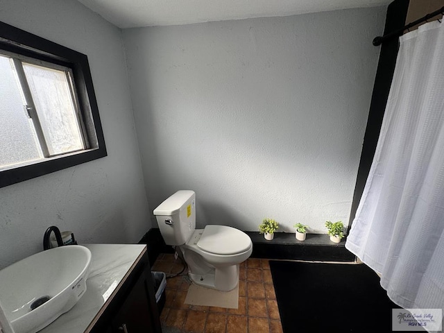 full bathroom with a textured wall, vanity, and toilet