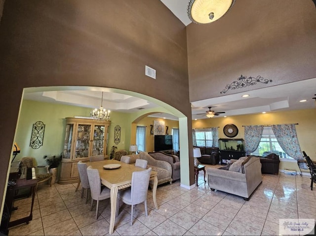 tiled dining space featuring ceiling fan with notable chandelier and a tray ceiling