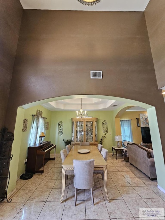 dining room featuring a chandelier, light tile patterned floors, a towering ceiling, and a raised ceiling