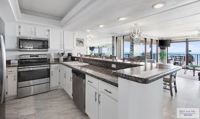 3000 Gulf Blvd, South Padre Island, TX 78597 - kitchen featuring stainless steel appliances, a peninsula, white cabinetry, dark stone counters, and light marble finish flooring