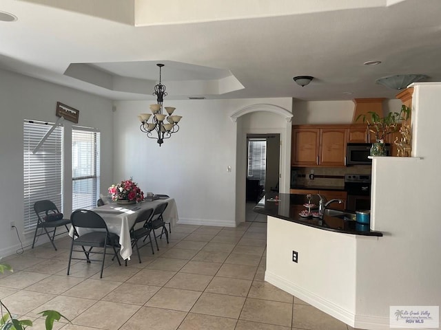 dining area with light tile patterned floors, a tray ceiling, an inviting chandelier, and sink