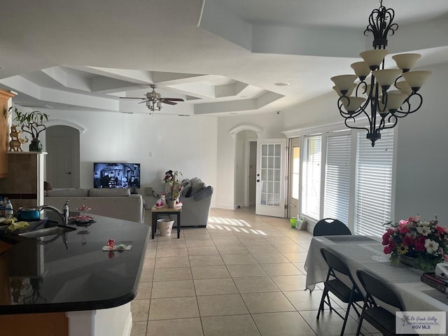 tiled dining space featuring a tray ceiling, sink, and ceiling fan with notable chandelier