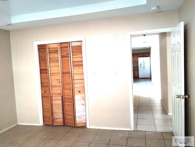 unfurnished bedroom featuring white fridge with ice dispenser, a closet, and light tile patterned floors