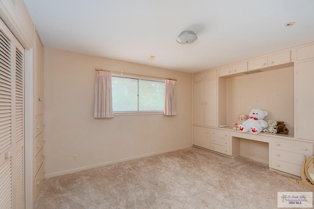 unfurnished bedroom with light carpet and built in desk
