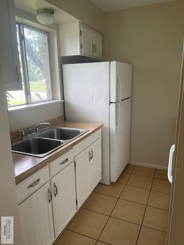 kitchen featuring light tile patterned flooring, white fridge, white cabinetry, and sink