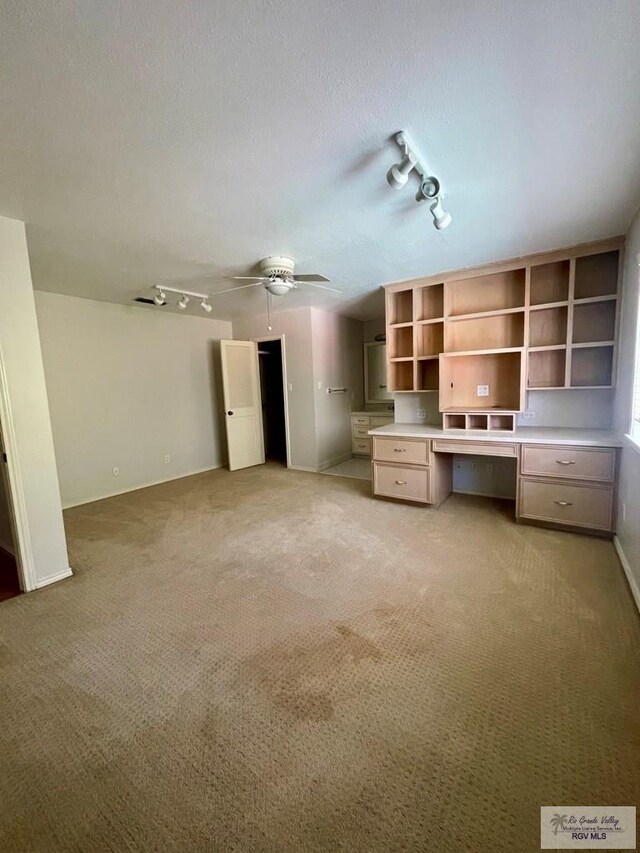 unfurnished living room with light carpet, track lighting, a textured ceiling, ceiling fan, and built in desk