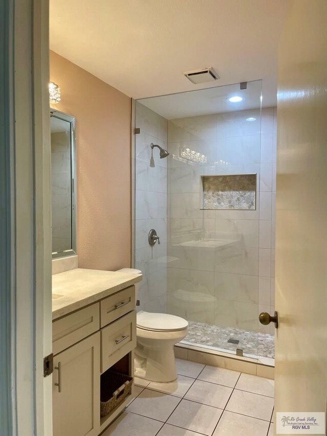 bathroom featuring tile patterned flooring, vanity, tiled shower, and toilet