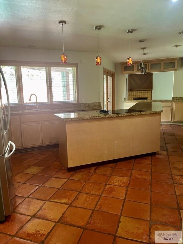 kitchen with stone counters, sink, stainless steel fridge, decorative light fixtures, and decorative backsplash