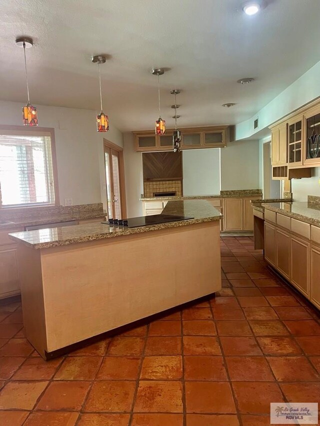 kitchen featuring light stone countertops, a center island, pendant lighting, and cream cabinetry