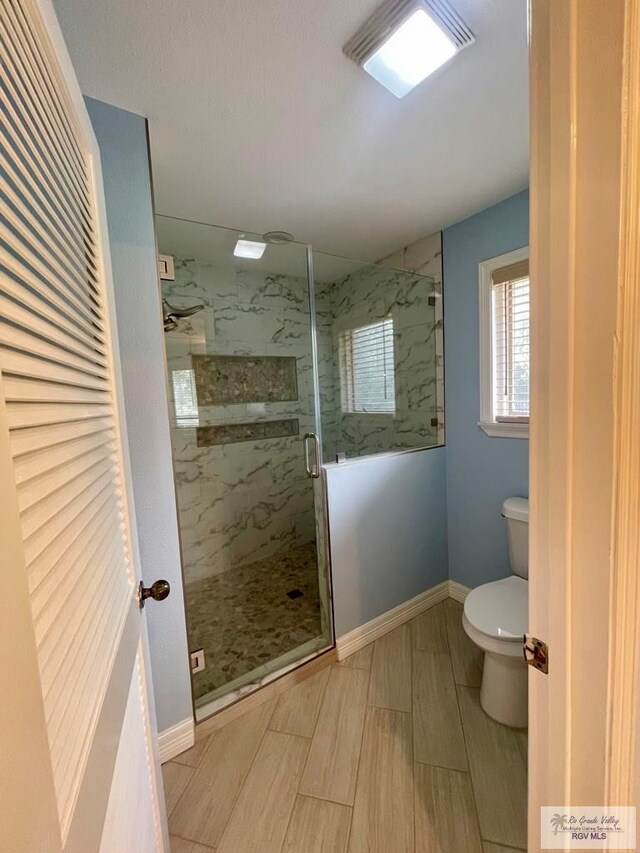 bathroom featuring a shower with door and toilet