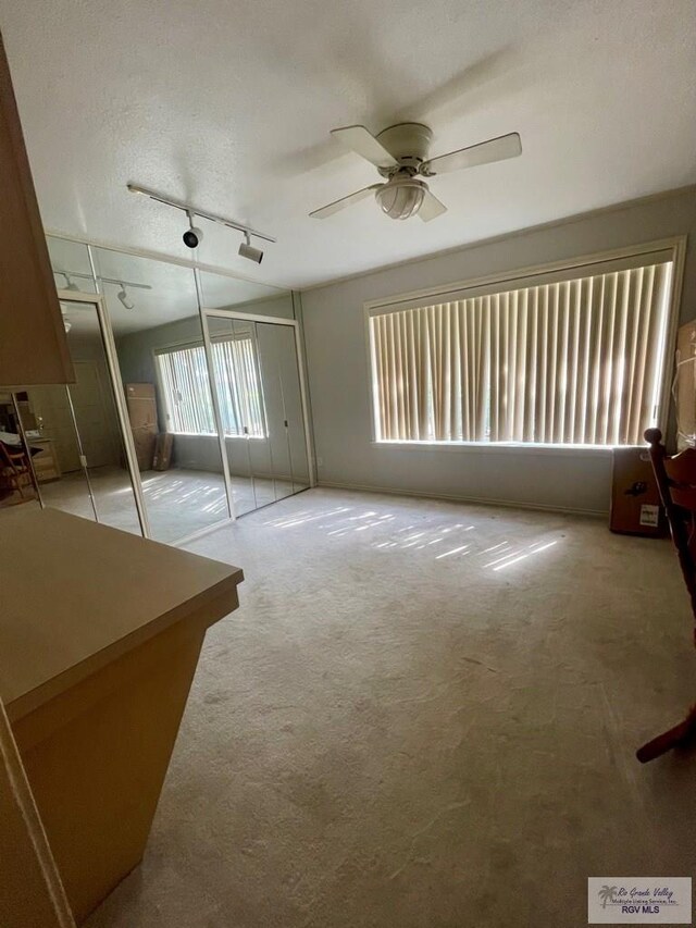 interior space featuring rail lighting, ceiling fan, a textured ceiling, and a closet