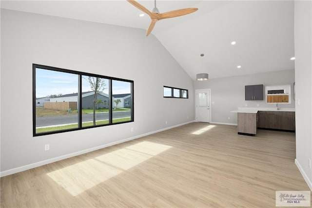 unfurnished living room featuring ceiling fan, sink, high vaulted ceiling, and light wood-type flooring