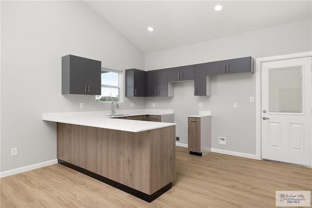 kitchen featuring kitchen peninsula, light wood-type flooring, high vaulted ceiling, and sink