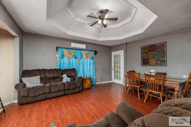 living room featuring an AC wall unit, ceiling fan, a raised ceiling, and wood finished floors