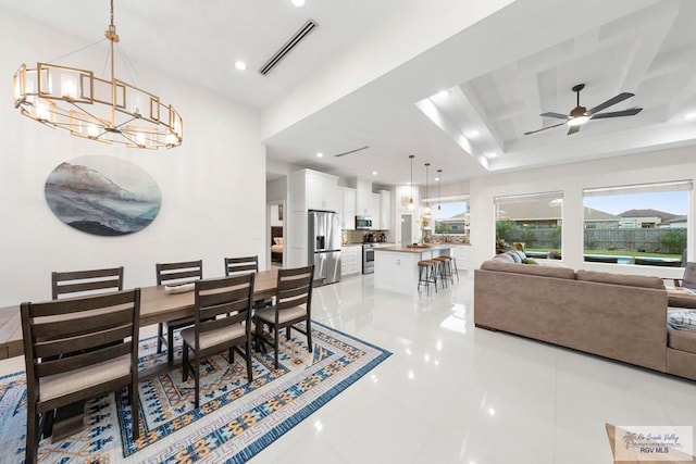 tiled dining space with a raised ceiling and ceiling fan with notable chandelier