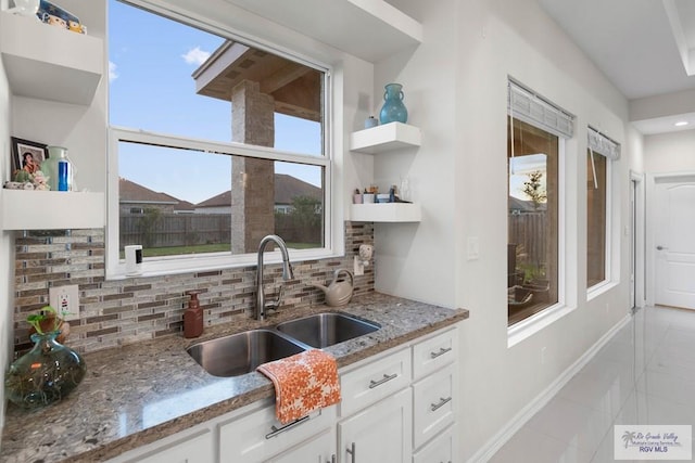 kitchen featuring plenty of natural light, backsplash, sink, stone countertops, and white cabinetry