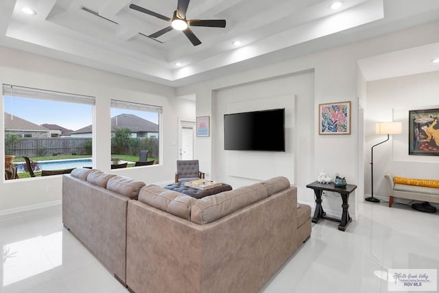 living room featuring a raised ceiling, ceiling fan, and light tile patterned flooring