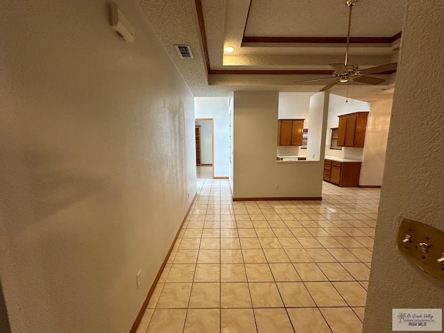 hallway featuring a textured ceiling, a raised ceiling, and light tile patterned flooring