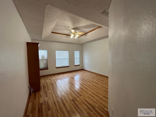 unfurnished room featuring hardwood / wood-style floors, ceiling fan, a textured ceiling, and a tray ceiling