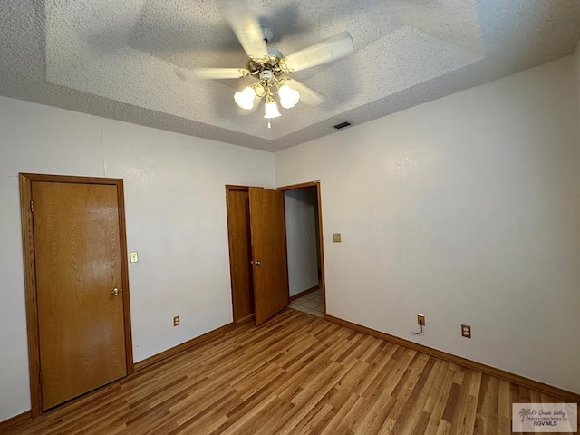 unfurnished bedroom featuring a textured ceiling, light hardwood / wood-style floors, ceiling fan, and a tray ceiling