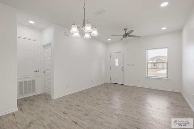 empty room featuring ceiling fan with notable chandelier and light wood-type flooring