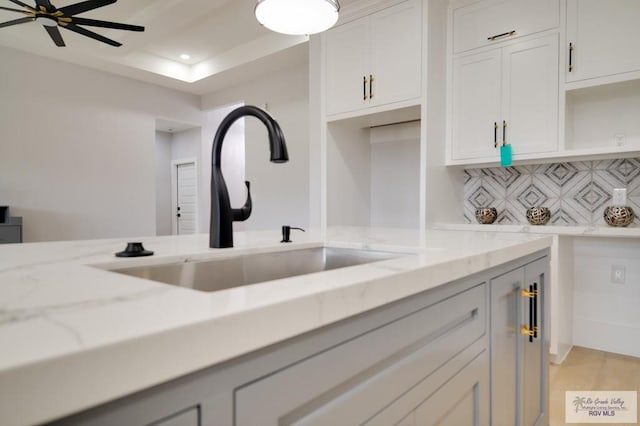 kitchen with decorative backsplash, light stone counters, white cabinetry, and sink